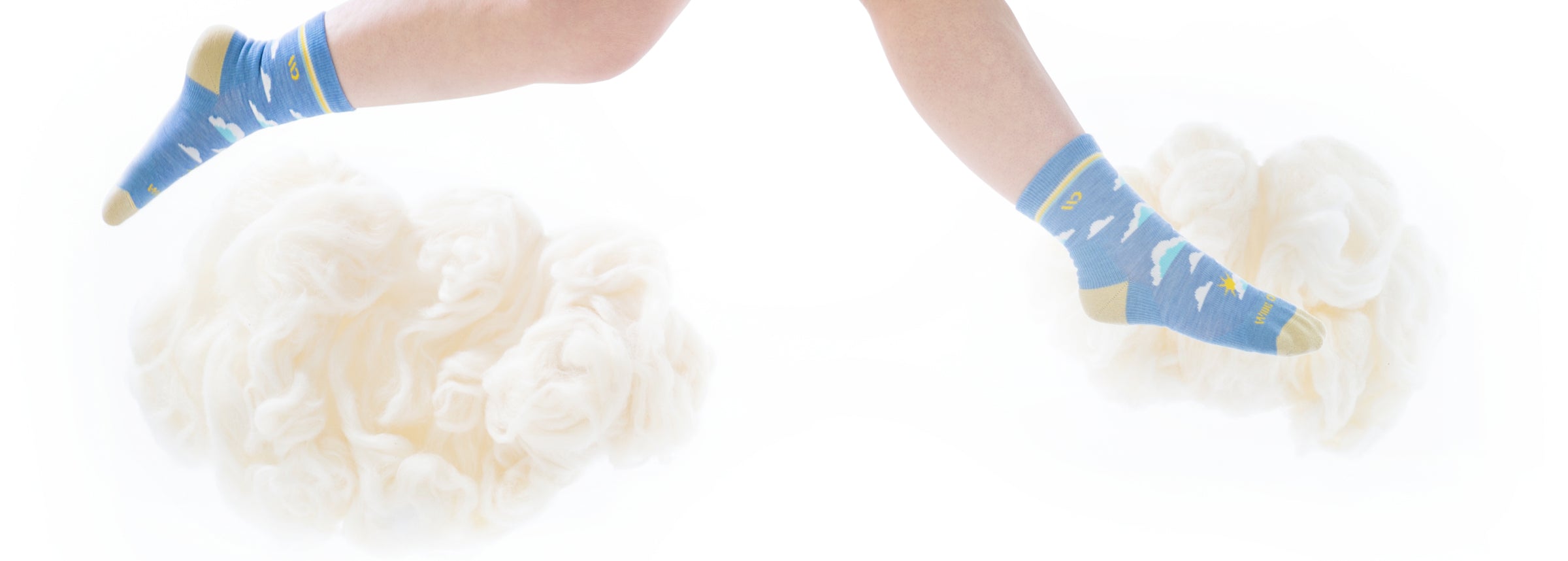 A pair of feet in Wide Open socks with at cloud design, jumping over fluffy merino wool clouds