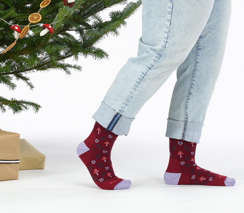 Close up of feet wearing clogs and burgundy socks with a floral and mushroom pattern