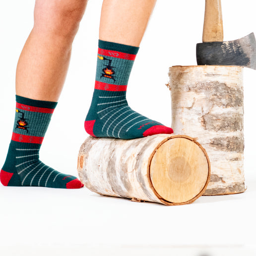 Feet wearing men's holiday socks showing a warm stove with a fire lit