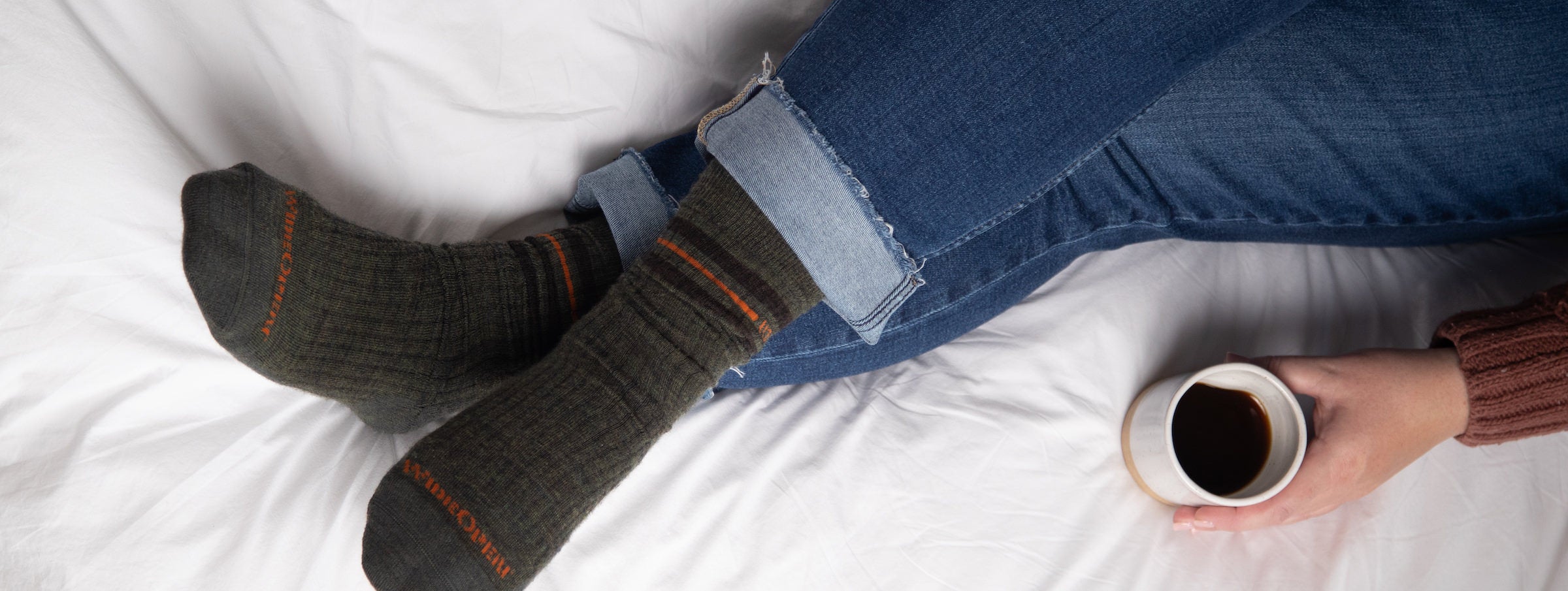 A person in bed, wearing jeans and Men's Vintage Stripe Cushioned Crew Socks in Forest
