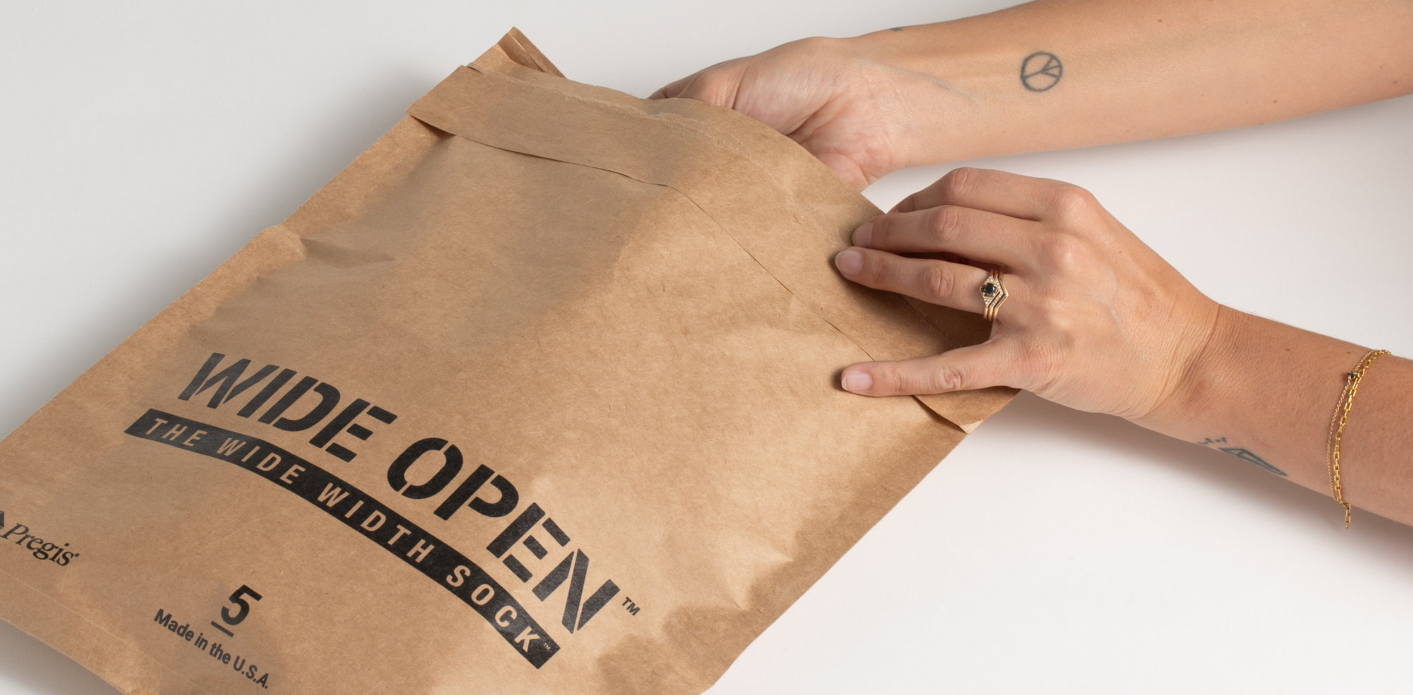 The back of a Wide Open brown shipping bag and a pair hands reaching into the bag