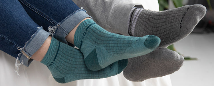 Two pairs of crossed feet wearing Wide Open socks in blue and gray