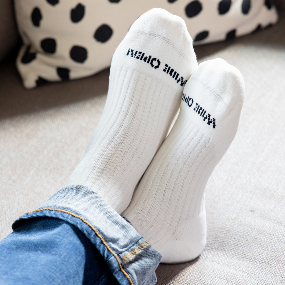 A pair of feet in Wide Open merino wool socks, white socks with a black logo on the toe