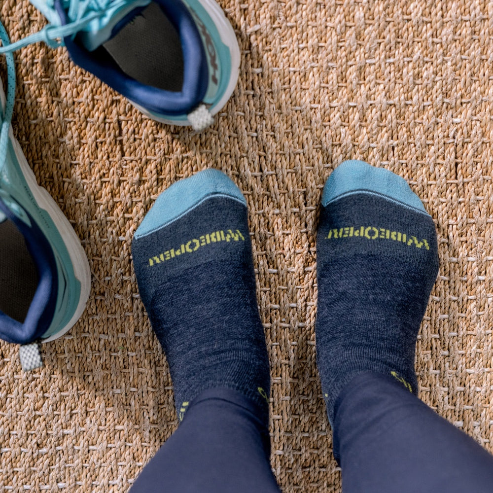 A pair of feet in blue Wide Open socks, their walking sneakers next to them