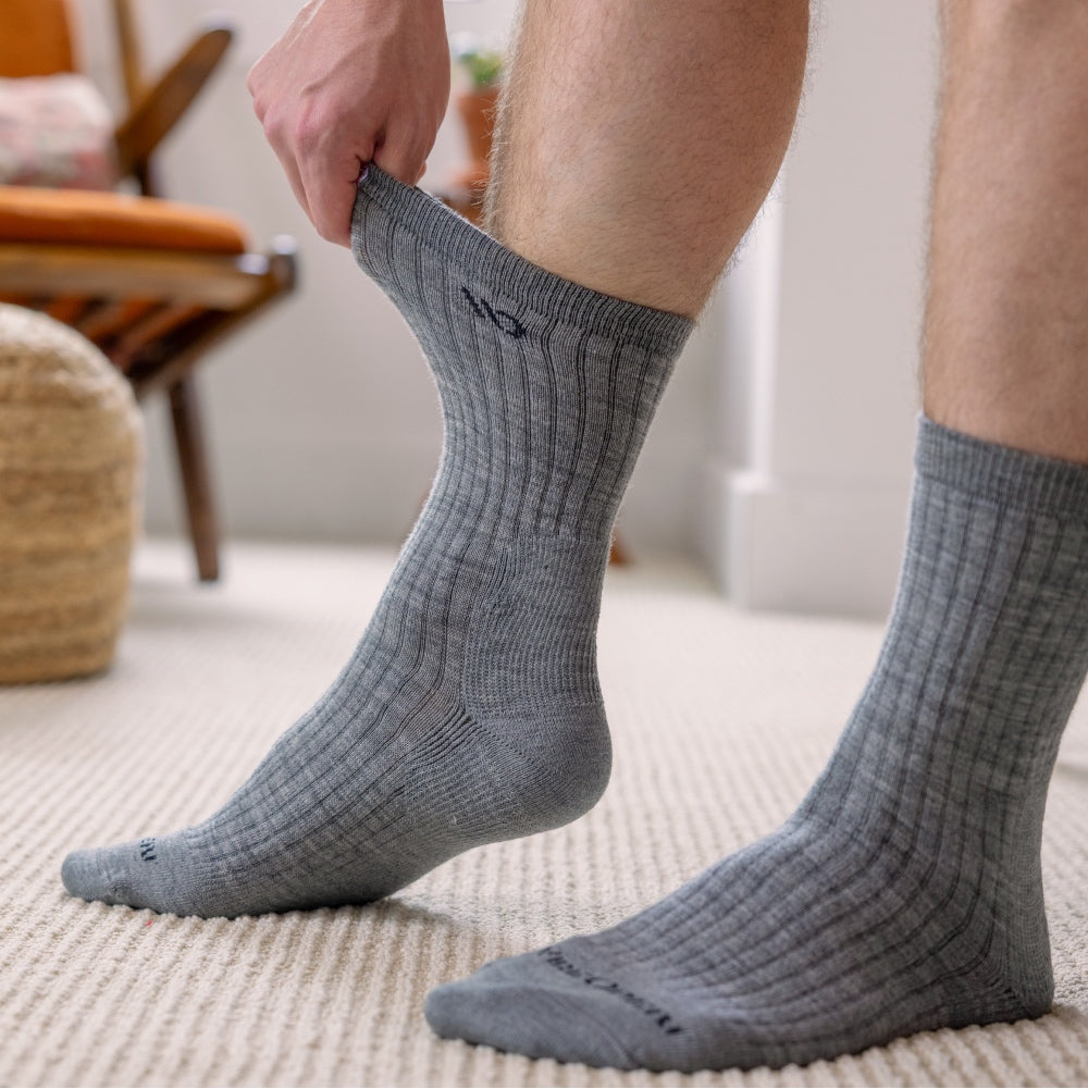 Feet wearing gray socks, a hand reaching down and pulling on the cuff to show how far they stretch