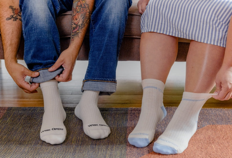 Two pairs of feet wearing white Merino Wool socks with a wide fit