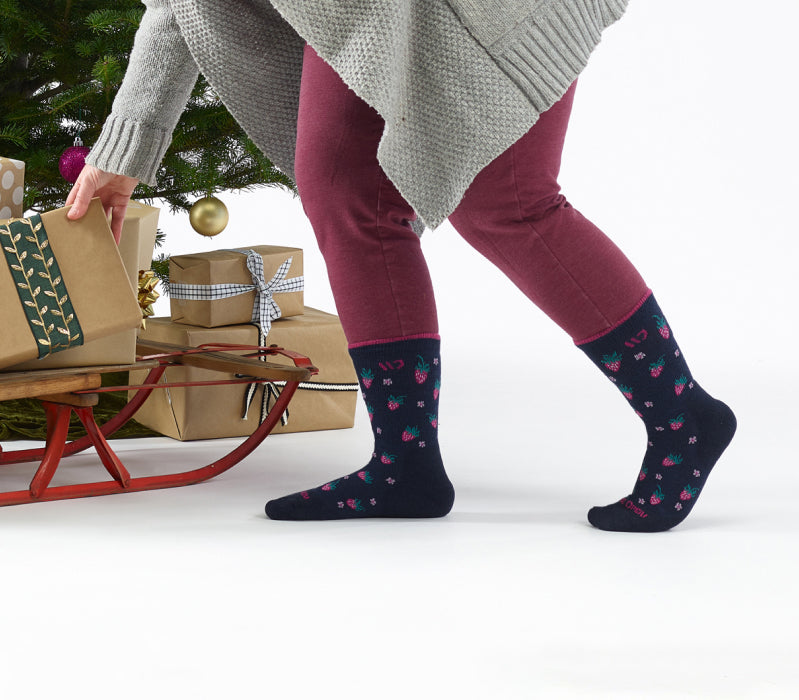 A person wearing Wide Open socks with strawberries on them, placing packages under a Christmas tree