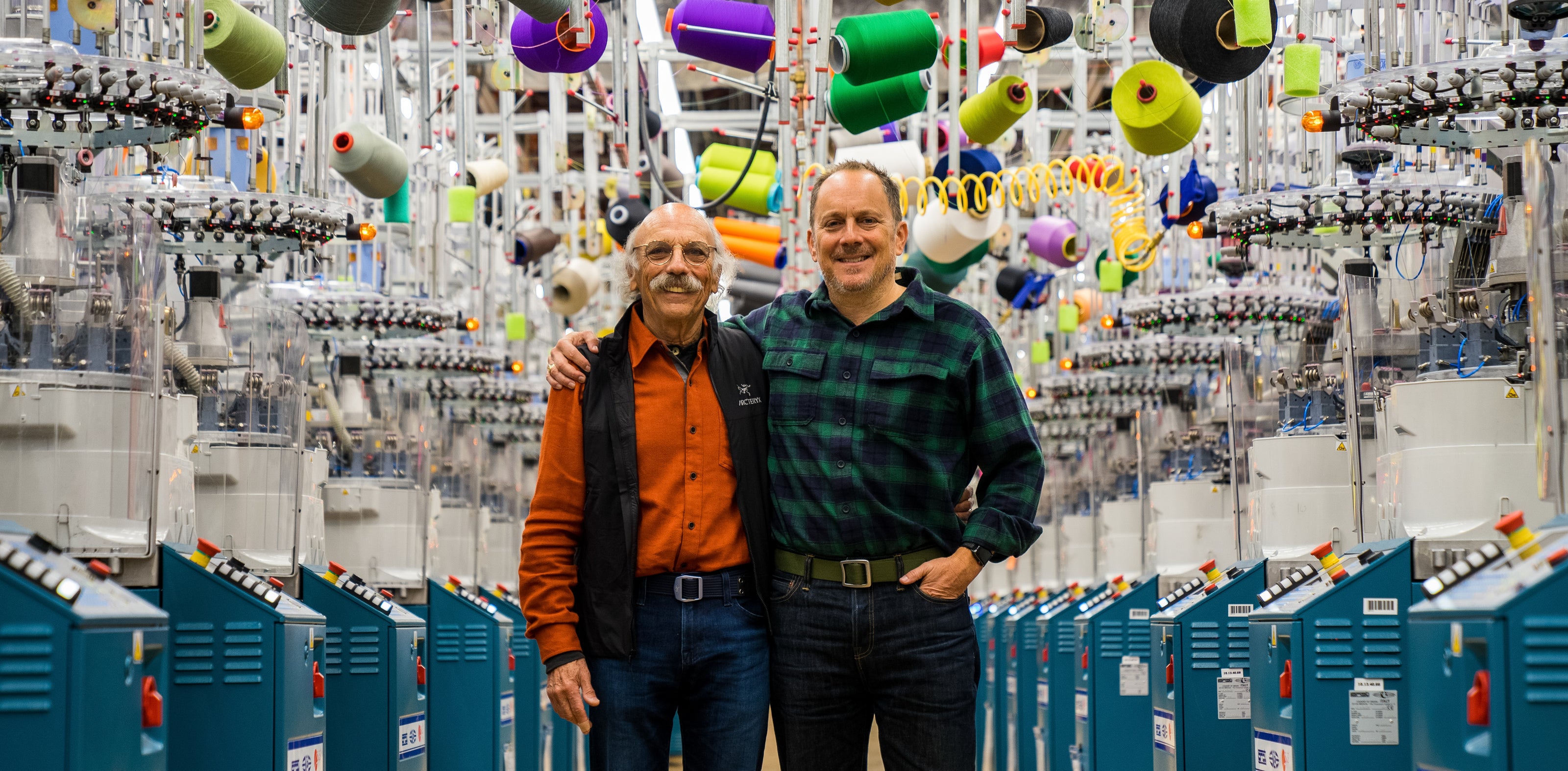 Two men with their arms around each other standing in a sock mill.
