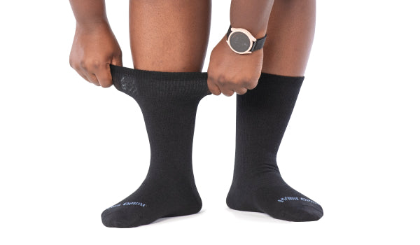 Feet wearing Wide Open women's crew height socks in black, pulling the cuff to show the stretch