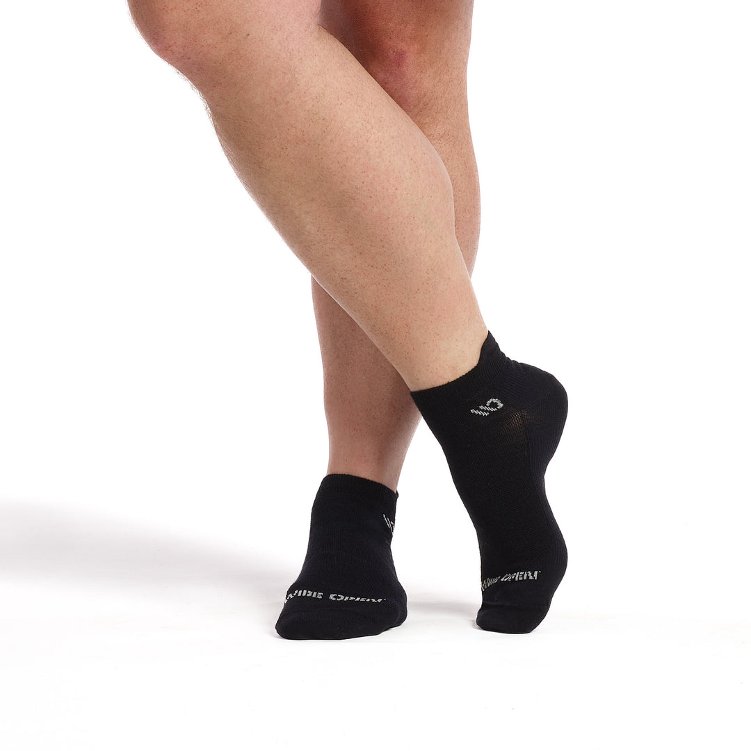 Models feet crosses wearing the 9013 solid lightweight ankle sock in black featuring a black body and gray logo