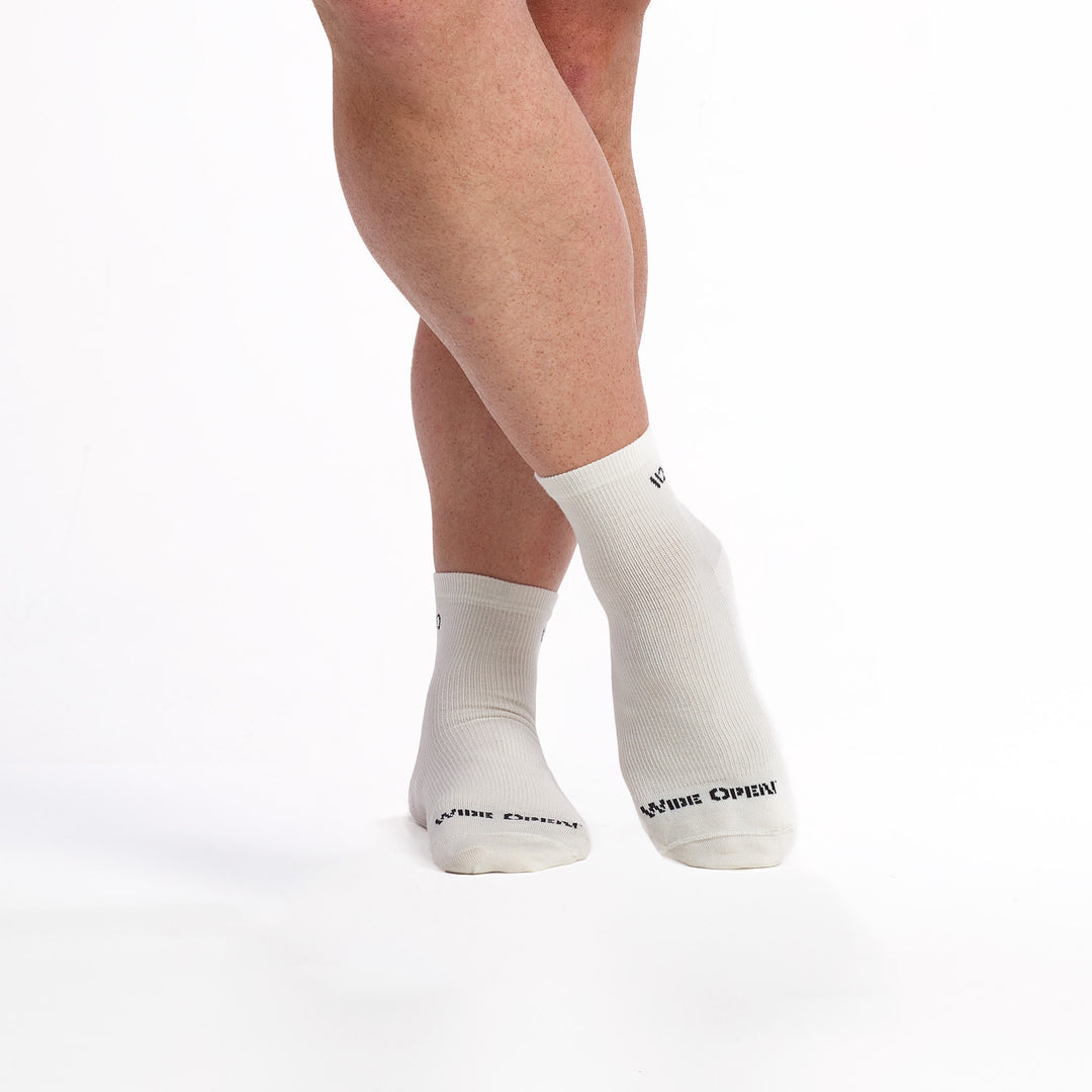 Models feet crossed wearing the men's 9014 solid lightweight quarter sock on white featuring the charcoal logo on toe