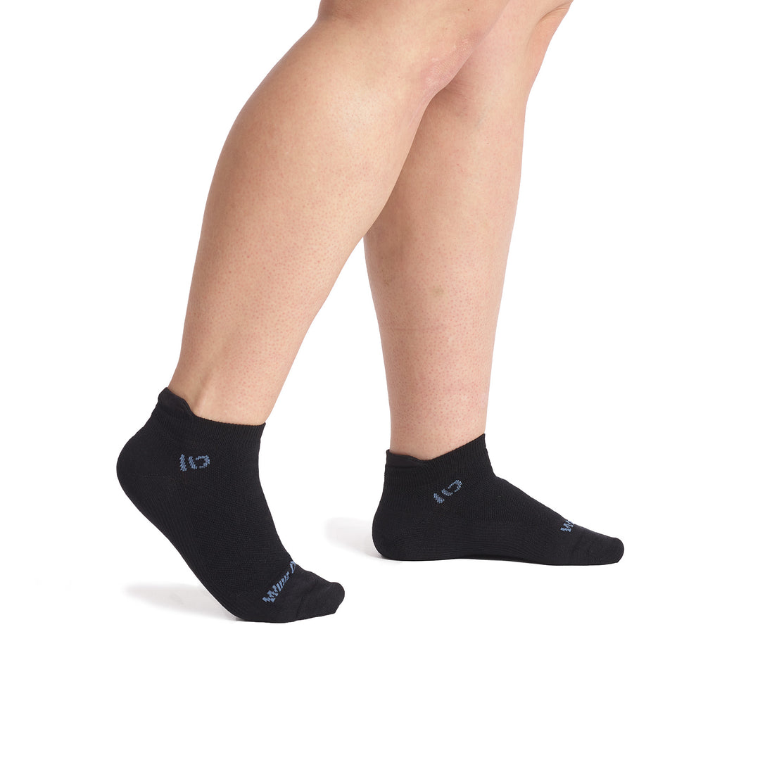 Model walking to the right with back foot lifted wearing the 9514 solid lightweight ankle sock in black featuring an all black body and periwinkle logo