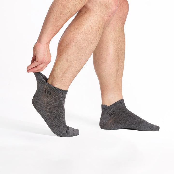 model stretching the back of left foot wearing the 9013 lightweight ankle sock in gray 