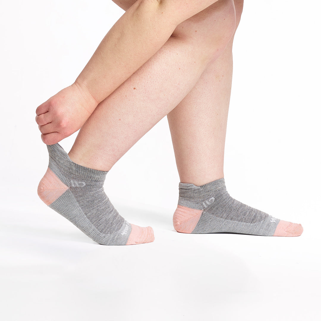 Model stretching the back of the sock wearing the 9514 lightweight ankle sock in light gray 
