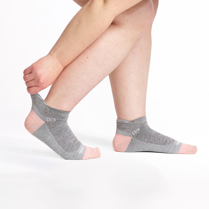 Model stretching the back of the sock wearing the 9514 lightweight ankle sock in light gray 