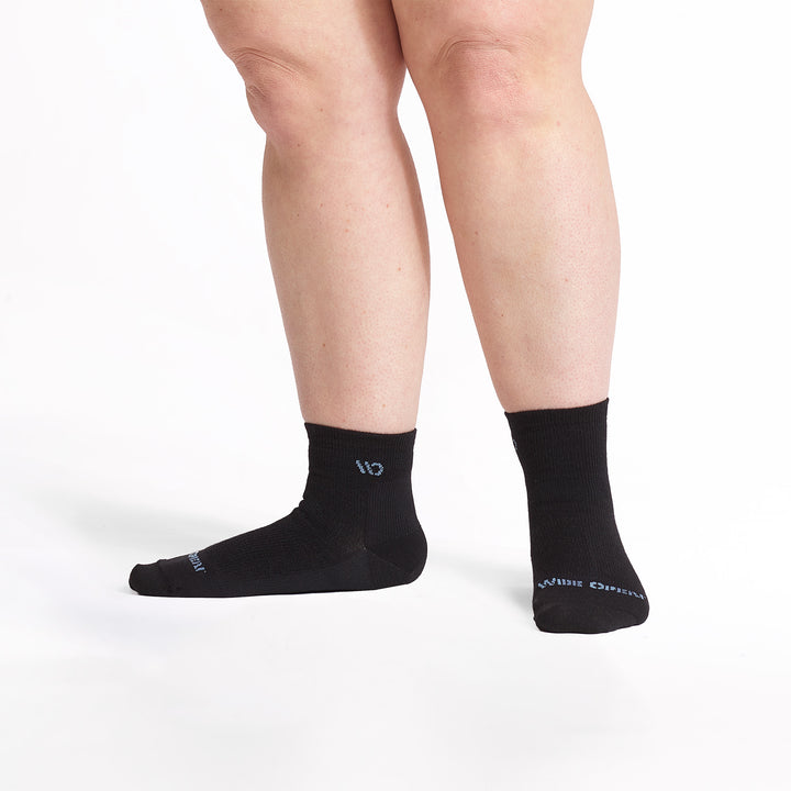 Models feet with left foot to the side wearing the 9515 lightweight quarter sock in black 